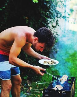 Shirtless man cooking food on barbecue grill