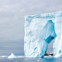 Iceberg in sea against cloudy sky