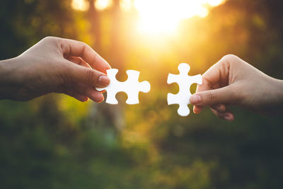 Cropped hands of women holding jigsaw pieces during sunset