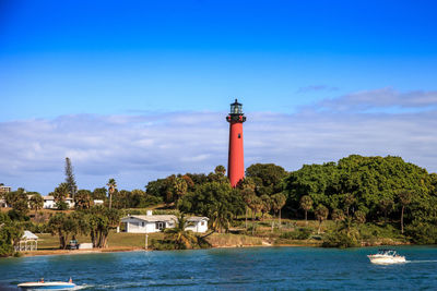 Lighthouse by sea and buildings against sky