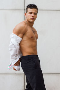 Portrait of muscular man removing shirt while standing against wall