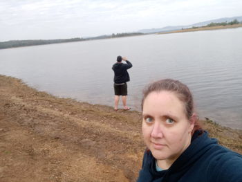 Portrait of man standing by lake against sky