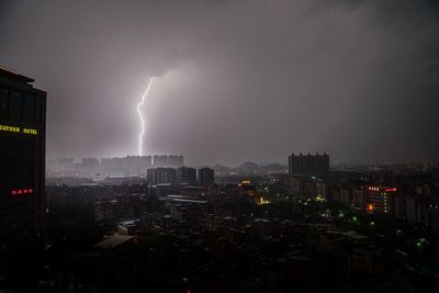 Buildings against lightning in cloudy sky at night