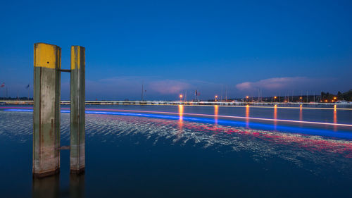 Light trails by sea against clear blue sky at night