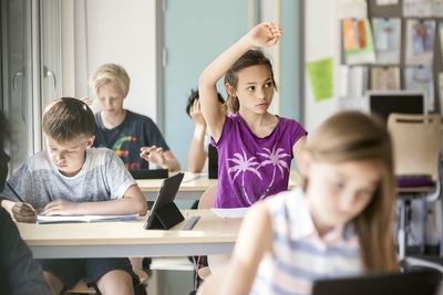 Schoolgirl raising hand at desk in classroom