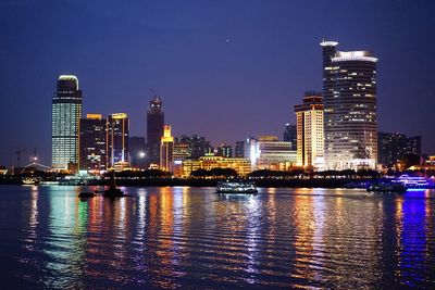 Illuminated buildings by river against sky in city at night