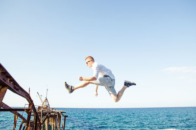 Side view full length of young man jumping over sea against sky