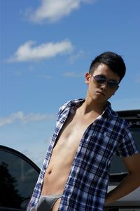 Portrait of man standing by car against sky