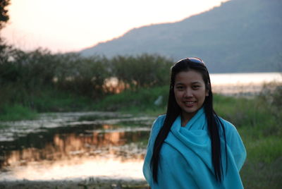 Portrait of young woman with long hair standing at lakeshore during sunset