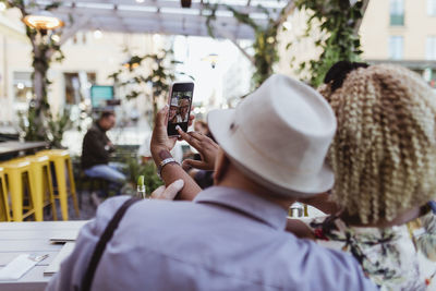 Rear view of senior couple taking selfie in sidewalk cafe