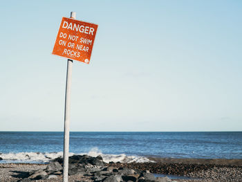 Information sign on beach against clear sky