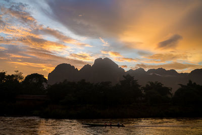 Scenic view of lake by silhouette mountains against orange sky