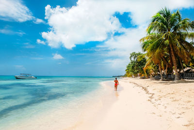 Rear view of woman walking at beach against sky