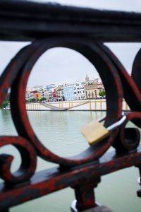 Close-up of railing by river in city against sky