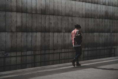 Rear view of man walking on footpath against wall