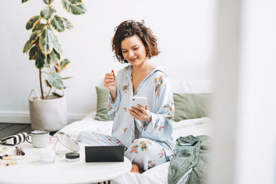 Portrait of young woman using mobile phone while sitting on table at home