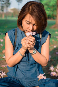 Woman smelling flower while sitting on field at park