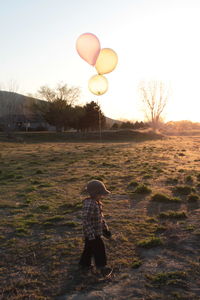 Side view of boy with transparent balloons on field against sky