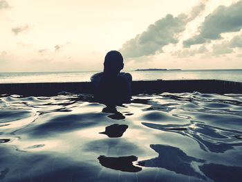 Man sitting at beach against sky during sunset