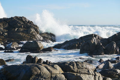 Waves splashing on rocks at shore against sky