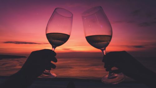 Close-up of hand holding glass of water against sunset sky