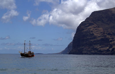 Sailboat sailing in sea by rock formations against cloudy sky