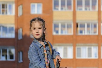 Cute girl looking away while standing against building