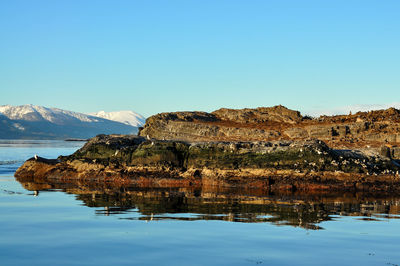 Rock formation in sea against clear sky during winter