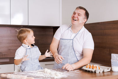 Happy smiling caucasian family in aprons cooking and kneading dough on a wooden