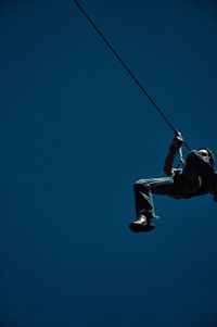 Low angle view of man on zip line against blue sky