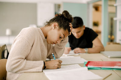 Teenage girl studying while sitting by male in classroom