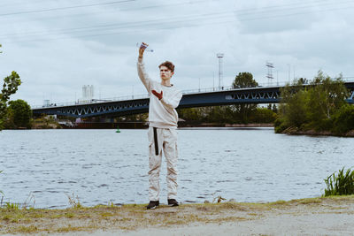 Full length of young man pouring water from bottle against sky