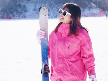Smiling young woman with snowboard standing on snow covered field