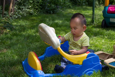 Cute boy playing with toy while sitting on grass outdoors