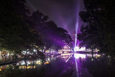 Illuminated trees by lake against sky at night