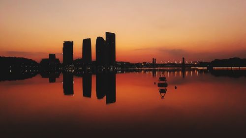 Scenic view of lake and buildings against sky during sunset