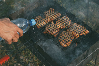 Cropped hand of person pouring water on barbecue grill