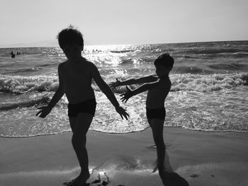Shirtless brothers gesturing while standing on shore at beach