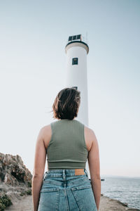 Rear view of woman standing on beach against clear sky