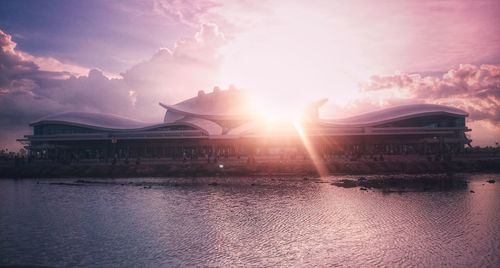 Built structure by river against sky during sunset