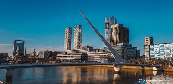 Bridge over river by buildings against clear sky