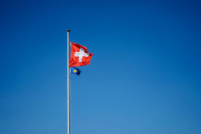 Low angle view of flags waving against clear blue sky