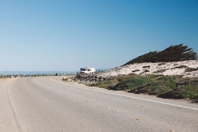 Road by sea against clear blue sky