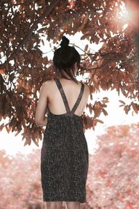 Portrait of woman in backless dress standing on leaves during autumn