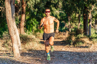 Full length of shirtless man running in forest