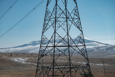 Electricity pylon on snow covered land against sky