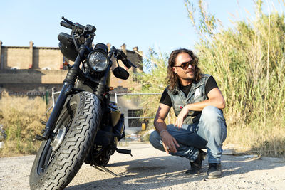 Full length of man crouching by motorcycle outdoors