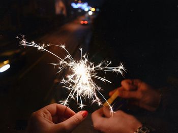 Cropped hands holding lit sparkler at night