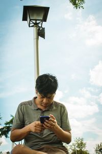 Full length of young man using mobile phone against sky