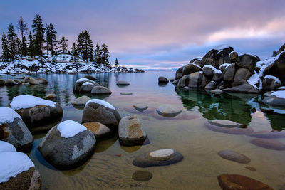 Rocks in sea against sky during sunset